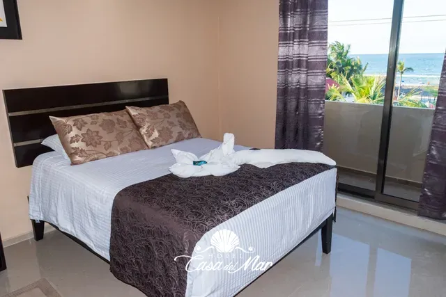 Cama matrimonial junto al ventanal del balcón, con el mar al fondo · Hotel Casa del Mar